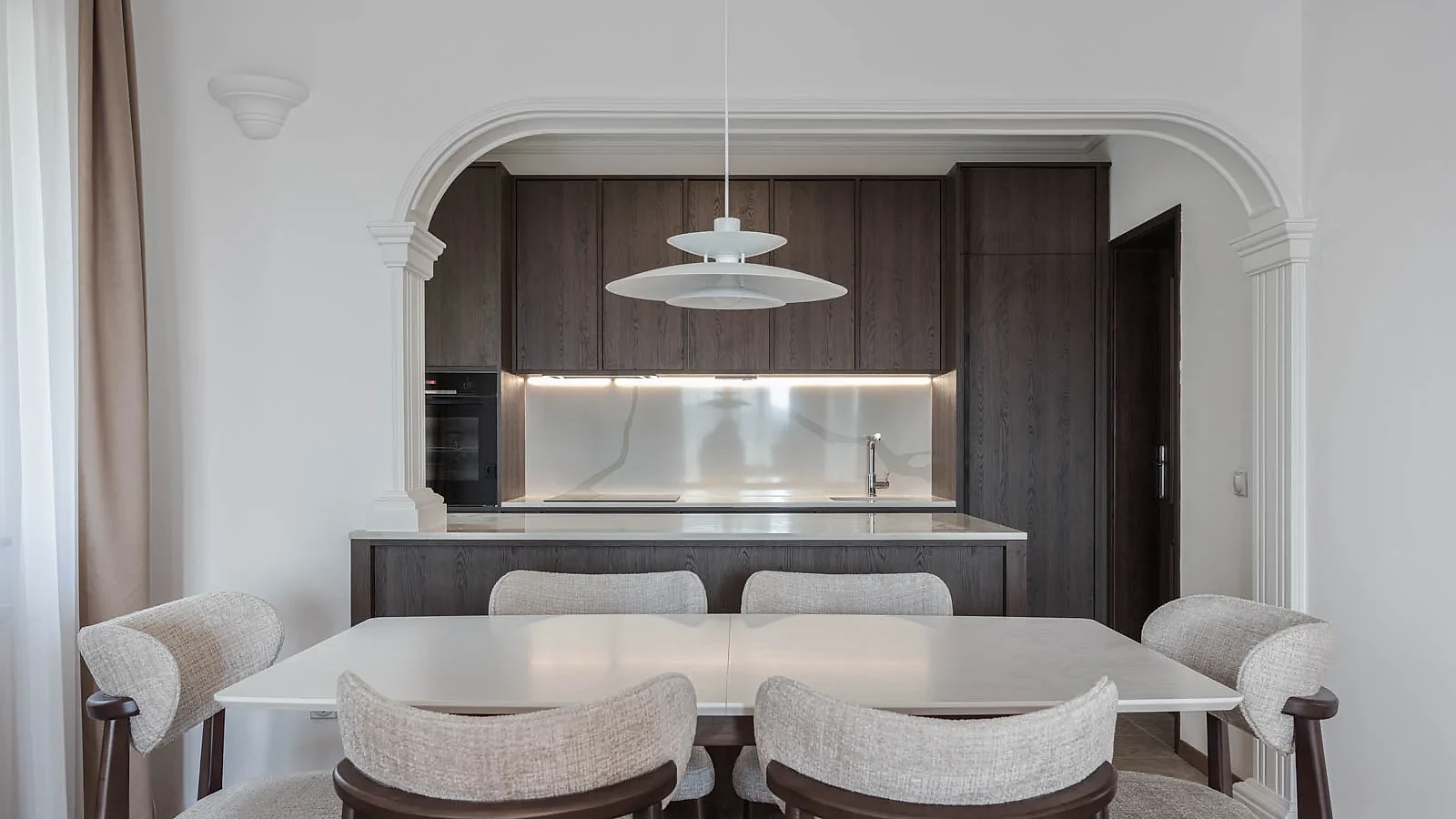 BP77 dining room with neutral chairs, dark oak cabinetry and an illuminated stone backsplash