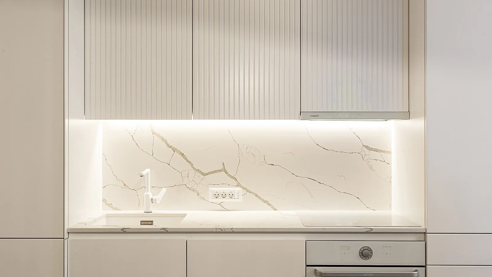 KMR kitchen with fluted white cabinetry and an illuminated stone backsplash