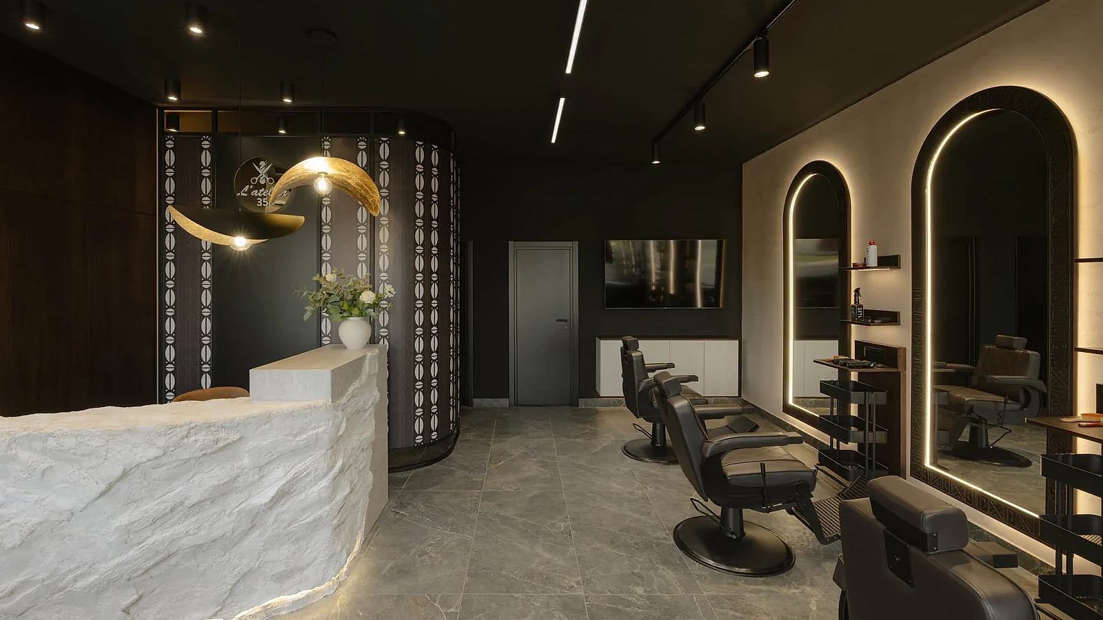 L'Atelier 35 hair salon interior with the stone reception desk and illuminated barber stations