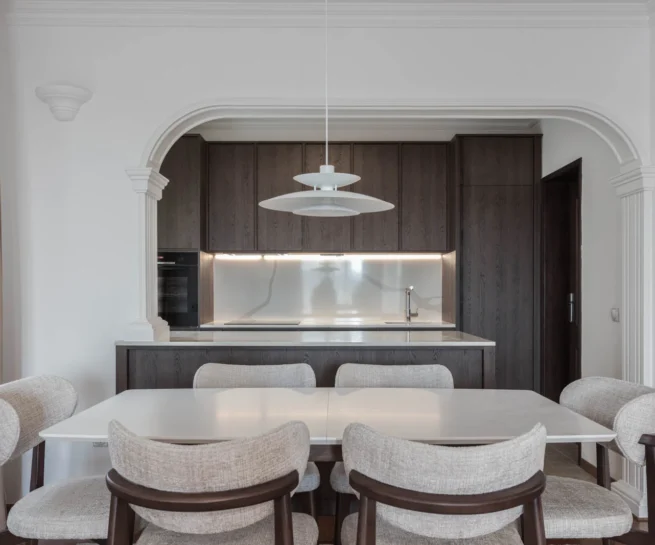 BP77 dining room with neutral chairs, dark oak cabinetry and an illuminated stone backsplash