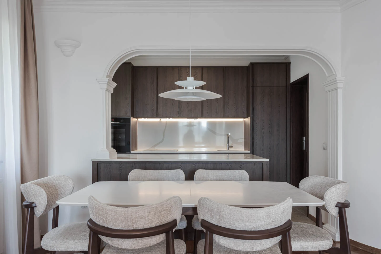 BP77 dining room with neutral chairs, dark oak cabinetry and an illuminated stone backsplash