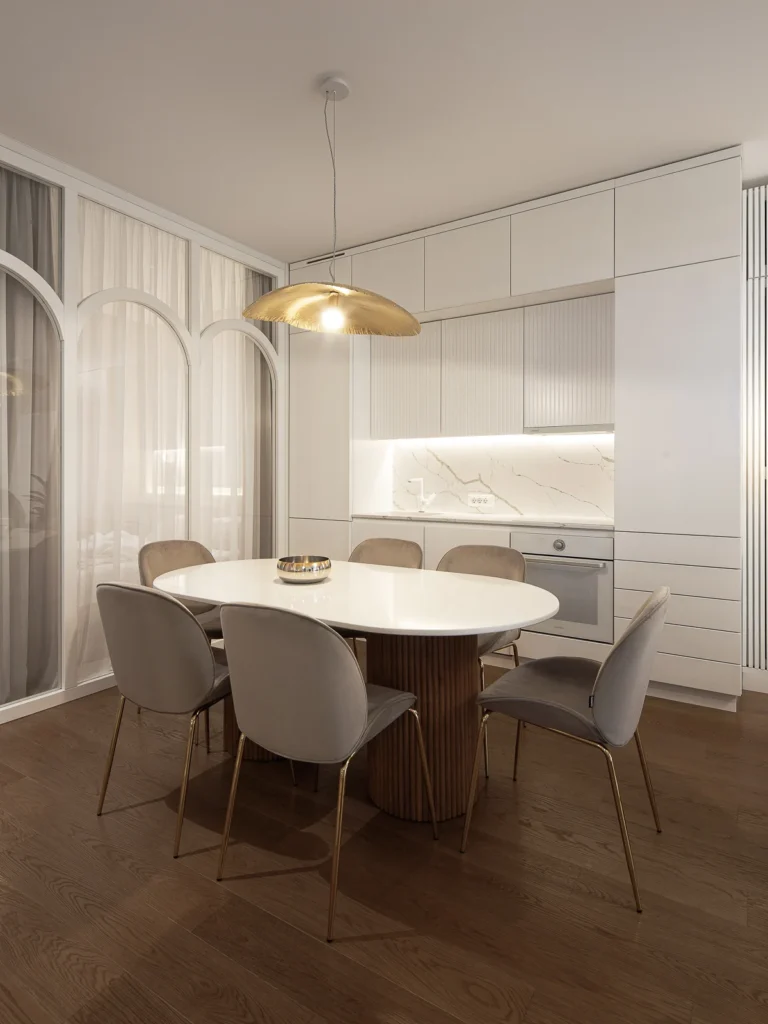 Oval dining table beneath a sculptural brass pendant in KMR Apartment