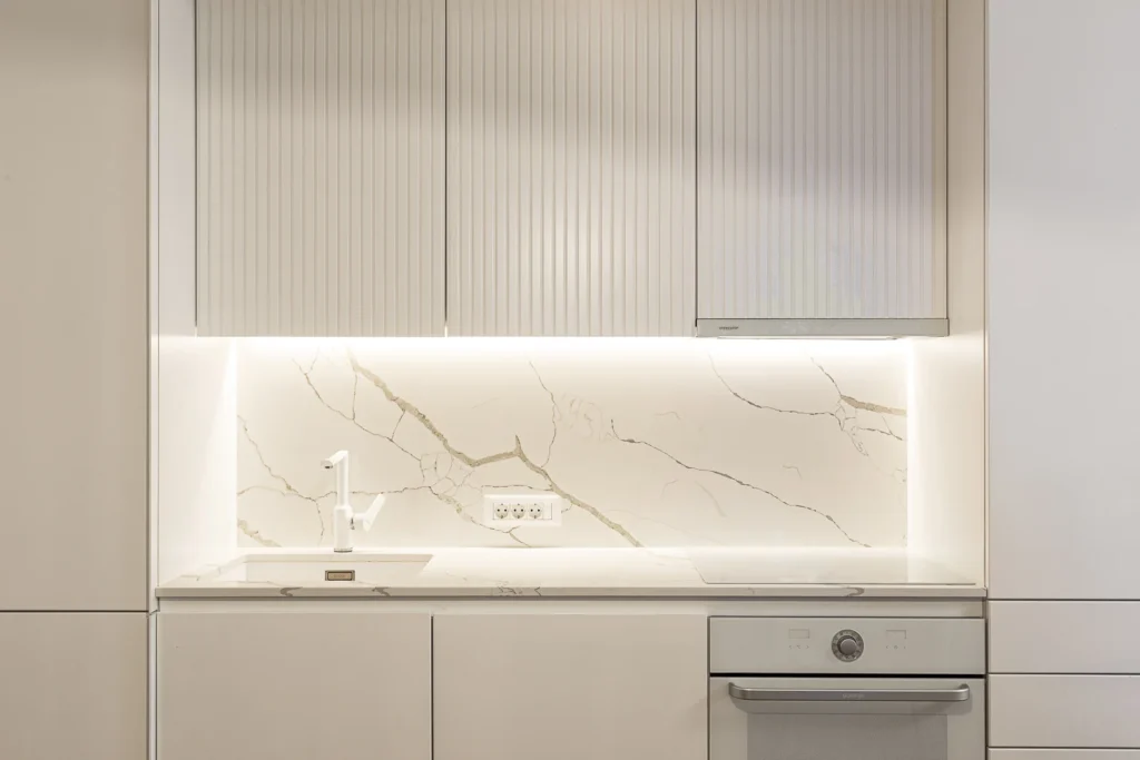 KMR kitchen with fluted white cabinetry and an illuminated stone backsplash