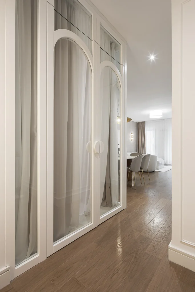 Glass-enclosed bedroom with arched timber frames and curtains in KMR Apartment