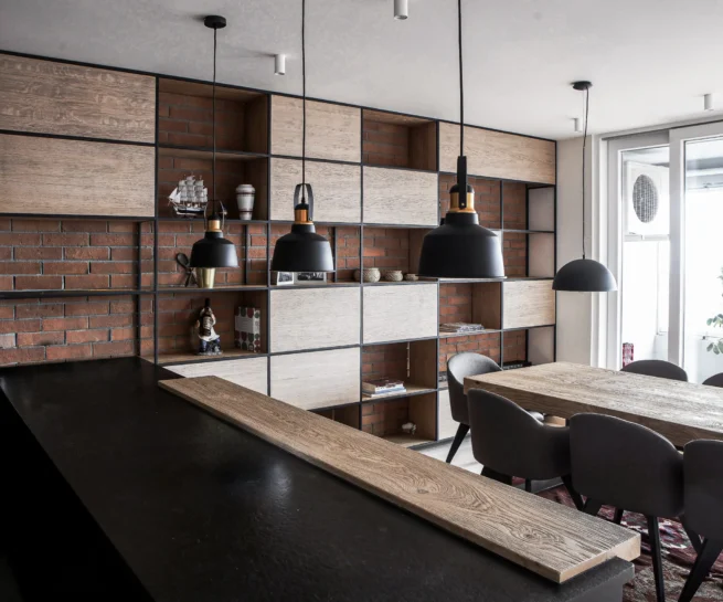 A75 Apartment open-plan kitchen and dining area with black cabinetry, exposed brick and warm wood