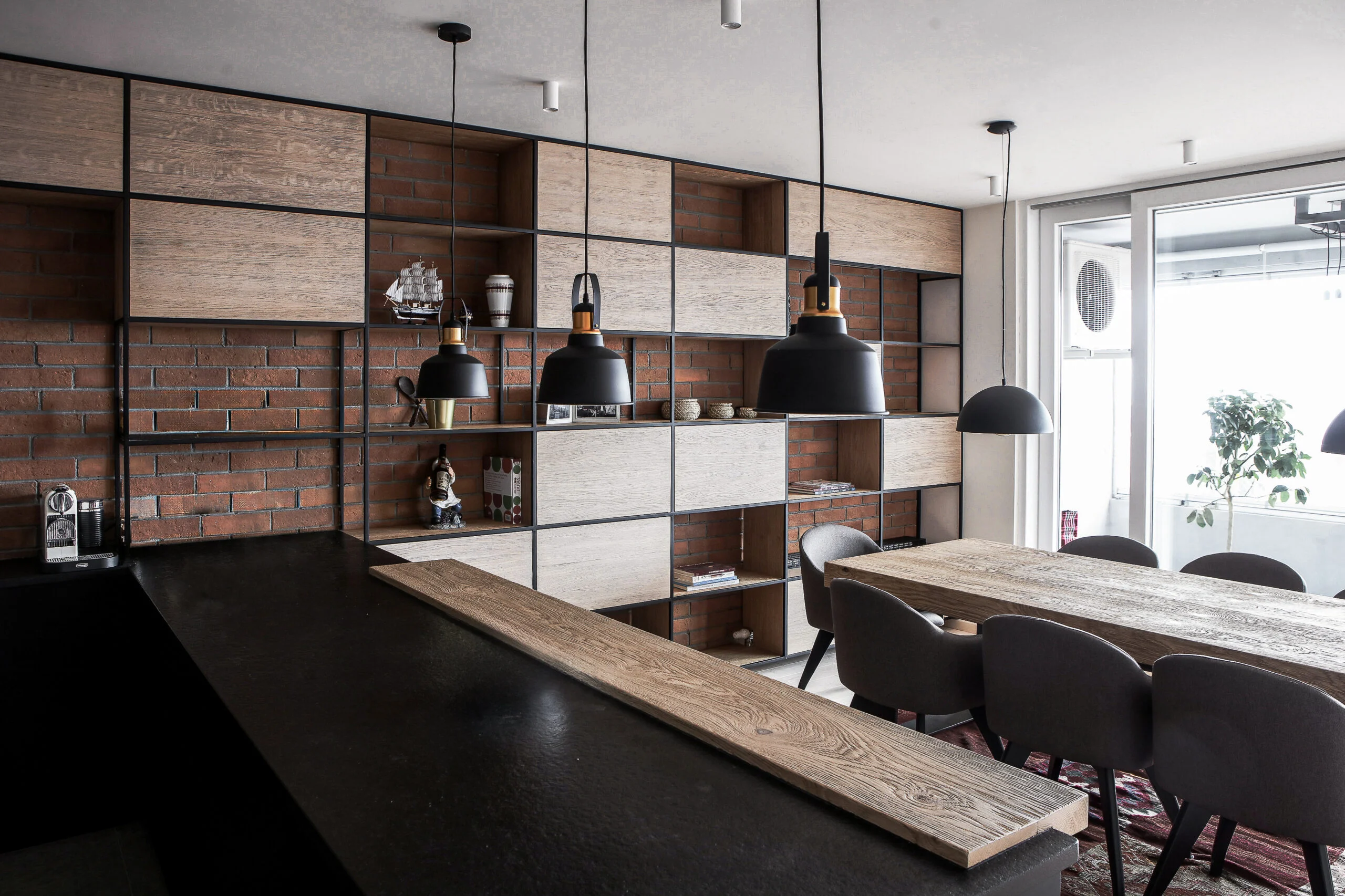 A75 Apartment open-plan kitchen and dining area with black cabinetry, exposed brick and warm wood
