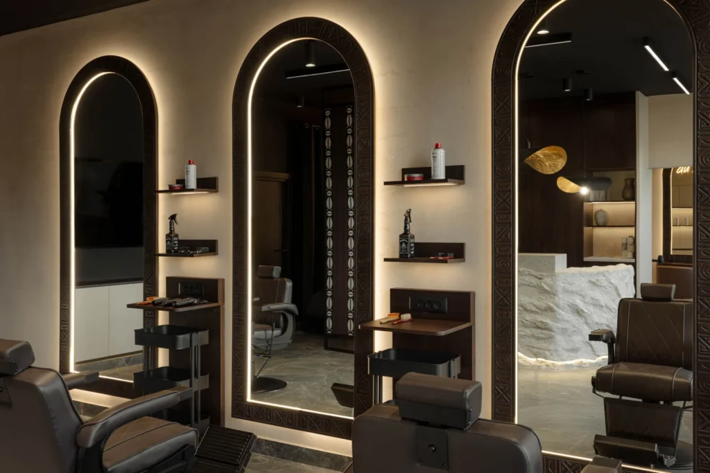 Barber chairs facing illuminated arched mirrors in the dark wood interior of L'Atelier 35
