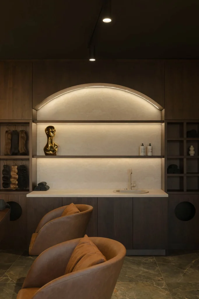Curved illuminated shelving and tan lounge chairs in the women's area at L'Atelier 35