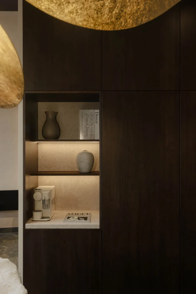 Custom dark wood storage niche beneath a sculptural brass pendant at L'Atelier 35