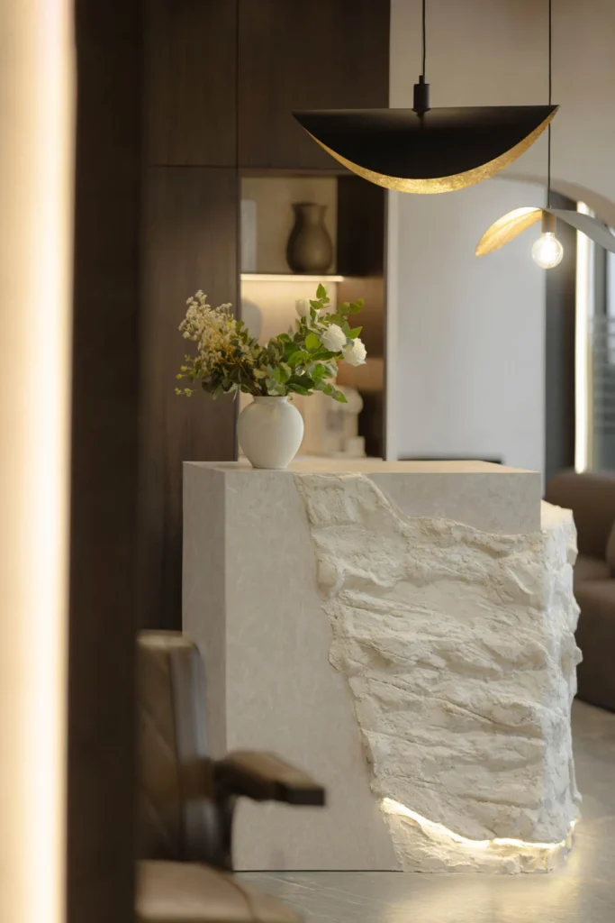 Textured stone reception desk with flowers beneath a sculptural brass pendant